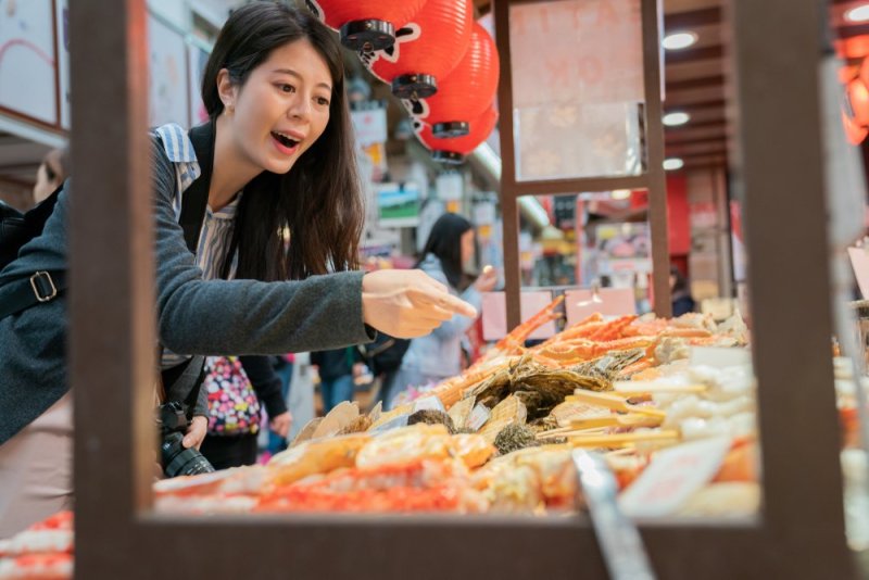Asian Tourist Reaching For Yakitori And Kushiyaki Meat Skewer In Kuromon Market